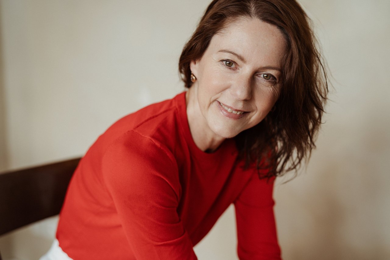 Gabriella Rist, Gründerin der GANESHASHALA® Trauma Fachakademie, lacht über eine Stuhllehne gelehnt in die Kamera